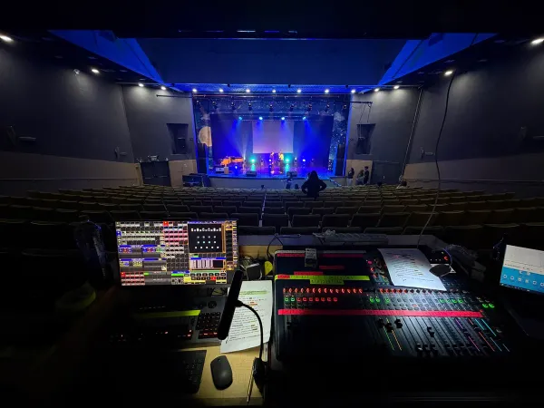 Control position in a darkened hall, stage lighting visible in the distance