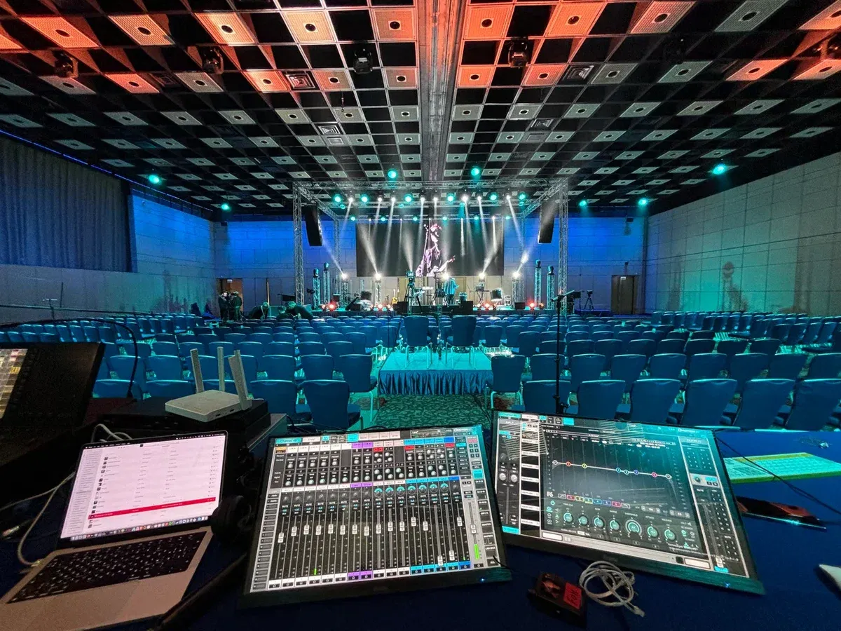 Front of house position with a mixing desk, facing a hall lit in blue with the stage in the distance